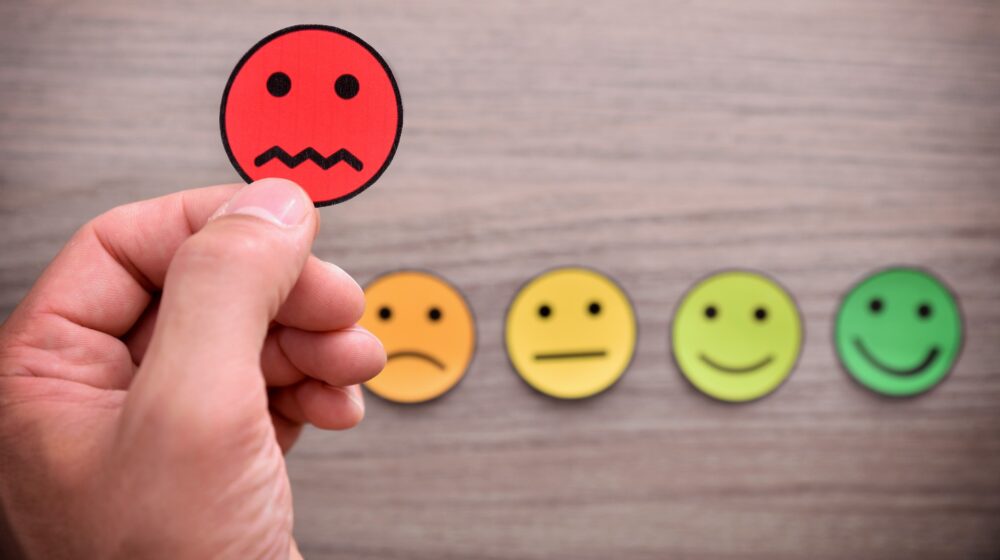How to respond to a negative review or feedback professionally - a hand holding a frowny face sticker